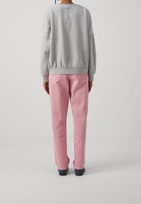 Sudadera gris con puños y dobladillo acanalados, combinada con pantalones de mezclilla rosa con un diseño de pierna recta y bolsillos traseros.