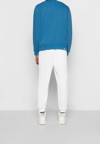 Felpa blu con scollatura rotonda e polsini a costine, abbinata a pantaloni della tuta bianchi. Caratterizzata da una vestibilità comoda e un discreto dettaglio del logo.