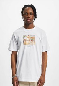 Camiseta blanca de algodón con un gráfico central colorido de bailarines cerca de edificios, con mangas cortas y un ajuste relajado.