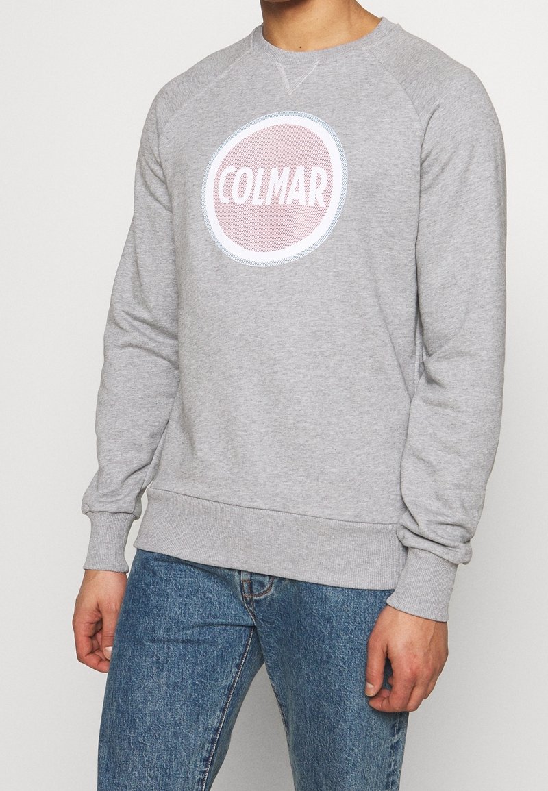 Felpa grigia con logo rotondo rosa con testo "COLMAR" in bianco, polsini a coste e scollatura a girocollo classica.