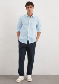 Lichtblauw button-up overhemd met een zak, met een subtiel patroon; gecombineerd met donkerblauwe broek en witte sneakers.