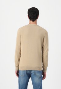 Beige gestrickter Pullover mit langen Ärmeln und rundem Hals, mit gerippten Bündchen und Saum, getragen mit hellblauen Jeans.