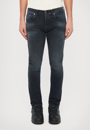 Jean en denim bleu foncé à coupe slim, doté de cinq poches, de quincaillerie en métal et d'un léger délavage. Assortis avec des baskets noires.