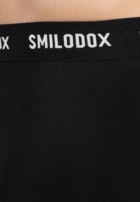 Czarny elastyczny pas w talii z białym logo "SMILODOX". Miękka tkanina, gładka faktura, zaprojektowana dla komfortu i elastyczności.