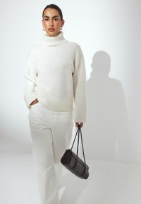 Balta megzta palaidinė su auk�štu kaklu, derinama su baltais kelnėmis; juoda stačiakampė rankinė su plonomis dirželių. Lygus tekstūra ir laisvas pritaikymas.