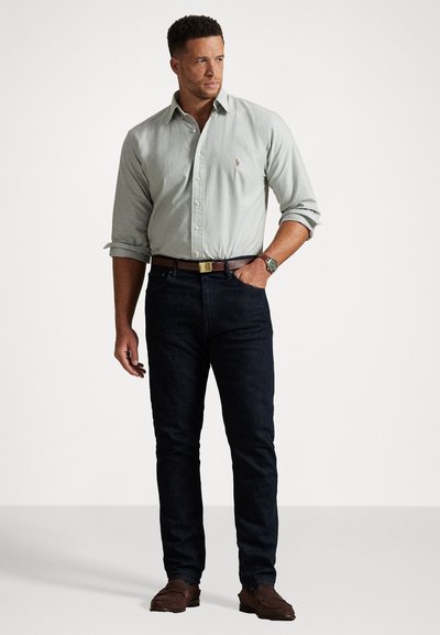 Šviesiai žalia marškinėlių su trumpomis rankovėmis palaidinė, tamsūs džinsai, rudas diržas ir rudos bateliai. Marškiniai turi mažą logotipą ant krūtinės, pasukamas rankoves ir laisvą siluetą.