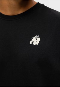 Zwarte sweatshirt met een witte afbeelding van een gorilla op de linkerkant van de borst. De stof lijkt zacht en glad met een ronde hals.