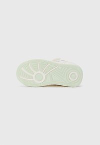 Semelle de sneaker de couleur claire avec une semelle extérieure en caoutchouc texturé, présentant une teinte verdâtre, des motifs circulaires et un design de bande de roulement détaillé.