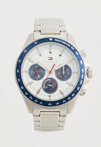 Sølv armbåndsur med hvid urskive, blå tachymeterskive, tre underdials der viser 24-timers format, dag og dato, samt rød sekundviser.