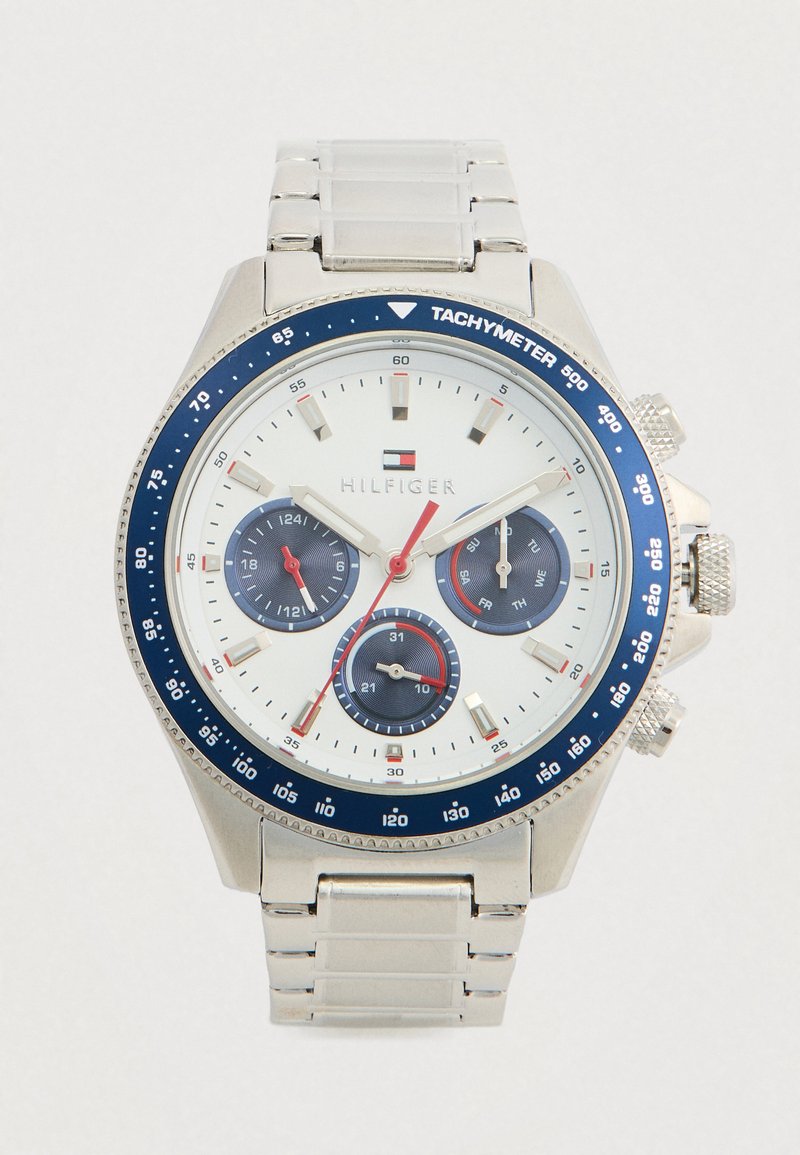 Sølv armbåndsur med hvid urskive, blå tachymeterskive, tre underdials der viser 24-timers format, dag og dato, samt rød sekundviser.