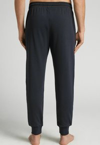 Dunkelgraue Baumwoll-Sweatpants mit lockerer Passform, elastischem Bund und gerippten Bündchen an den Knöcheln. Sanfte Textur ohne sichtbare Muster.