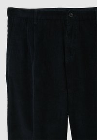 Dunkelblaue Cordhosen mit vertikaler Rippstruktur, ausgestattet mit Knopfverschluss, Gürtelschlaufen und Seitentaschen. Weiche Textur und strukturierte Passform.