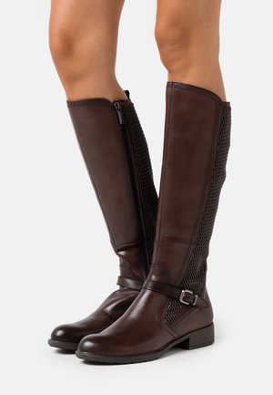 Stivali alti fino al ginocchio in pelle marrone con un pannello in rete testurizzata, zip laterale e una tracolla con un dettaglio in metallo. Tacco basso impilato.