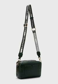 Zelená kožená crossbody taška s texturou, obdélníkového tvaru s přední kapsou, zdobená vzorovaným nastavitelným popruhem a stříbrnými kovovými doplňky.