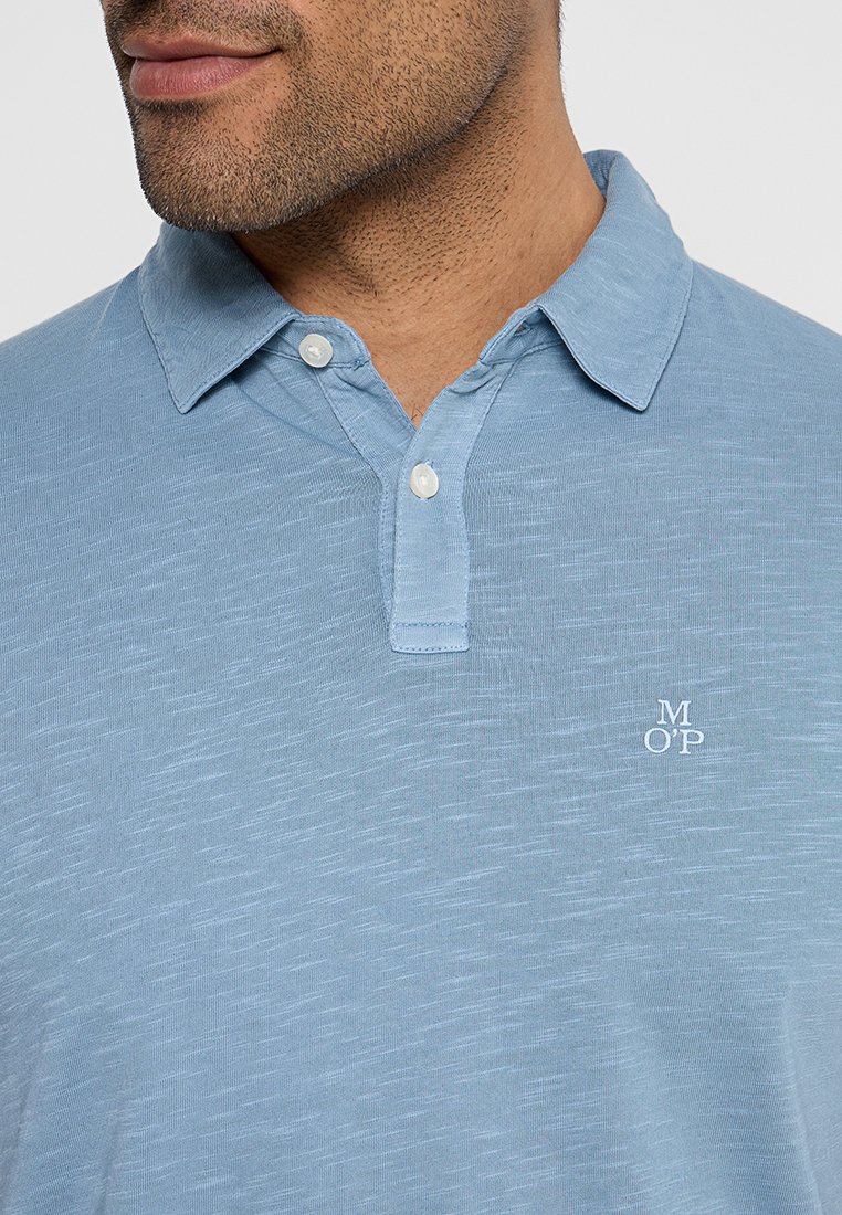 Himmelblaues Polohemd aus strukturiertem Stoff, mit einer Knopfleiste mit drei Knöpfen, kurzen Ärmeln und einem kleinen weißen Logo auf der Brust.