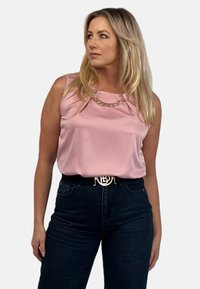 Różowy satynowy top bez rękawów z okrągłym dekoltem, w połączeniu z ciemnymi dżinsami i czarnym paskiem z złotą klamrą z logo.
