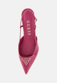 Vaaleanpunainen patenttinahkainen slingback-kengä, jossa on terävä kärki ja kultainen kolmion muotoinen logo. Liukas pinta ja kapea nilkkahihna.