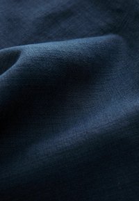 Tela tejida de color azul oscuro con una textura sutil, mostrada en pliegues suaves que resaltan el fino tejido y la superficie lisa del material.