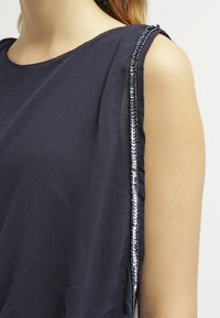 Débardeur bleu marine sans manches en tissu doux, avec une bordure en sequins le long de la couture de l'épaule pour un détail supplémentaire.