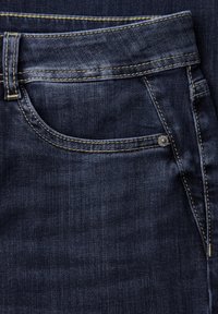 Primer plano de jeans de mezclilla azul oscuro mostrando el bolsillo delantero, la trabilla del cinturón y detalle de costura amarilla.