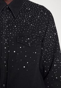 Black denim shirt featuring scattered clear rhinestones, two front pockets, and snap buttons, showcasing a textured, embellished design.