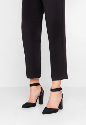 Czarne szpilki z ostrym noskiem, z satynowym wykończeniem i paskiem wokół kostki z kontrastującymi pomarańczowymi wykończeniami. Słupkowy obcas.