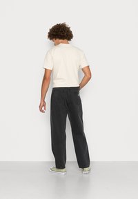 Light beige short-sleeve t-shirt paired with black straight-leg jeans; jeans have a back pocket detail and are worn with green sneakers.