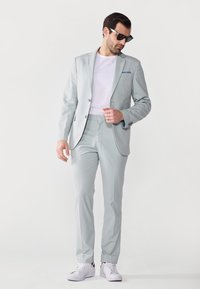Costum gri deschis cu o croială slim, asortat cu un tricou alb și adidași albi. Sacoul are un nasture și rever înformate.