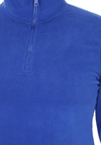 Kék bolyhos pulóver félig cipzárral. Puha tapintású, könnyű és sima felülettel rendelkezik. A cipzár közelében varrási részlet található.