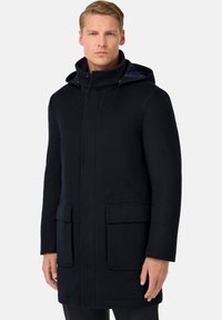 Temno modro dolg plašč s kapuco, izdelan iz gladkega materiala. Ima dve sprednji žepni nalepki in minimalističen dizajn.