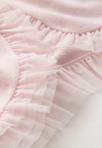 Gaiši rozā audums ar mīkstu faktūru un caurspīdīgiem volānu akcentiem ap malu, radot smalku daudzslāņu izskatu.