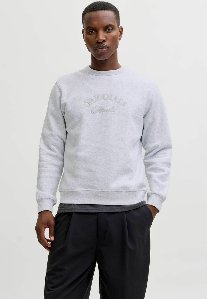 Grijze crewneck sweatshirt van een katoenmix, met geborduurd "ORIGINALS" logo. Gecombineerd met zwarte geplooide broeken, met subtiele textuur.