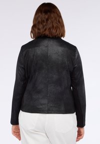 Svart jacka med en strukturerad yta, utrustad med långa ärmar och en skräddarsydd passform, kombinerad med ett mjukt material vid sidorna.