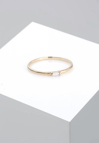 Goldener Ring mit einem dünnen Band und einem kleinen, rechteckigen, klaren Stein in der Mitte. Glatte, polierte Oberfläche mit minimalistischem Design.