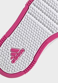 Bílá gumová podrážka boty s texturovaným povrchem, růžové akcenty podél okrajů a štítek "NEZANECHÁVÁ" s logem Adidas.