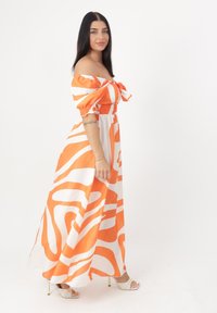 Maxikleid mit schulterfreien Ärmeln, orange-weißen Wellenstreifen, strukturierter geraffter Brustpartie und fließendem Rock. Sandalen mit klobigen Absätzen.