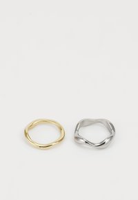 Dos anillos metálicos uno al lado del otro: un anillo de oro pulido y suave, y un anillo de plata con un diseño irregular y retorcido. Ambos son simples en su forma.