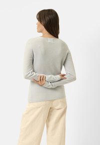Jasnoniebieski, miękki sweter z długimi rękawami i okrągłym dekoltem, noszony z kremowymi spodniami o szerokich nogawkach. Minimalistyczny design, bez wzorów.