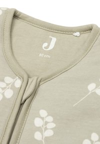 Combinaison en coton vert clair avec un motif de feuilles blanches, fermeture éclair et étiquette imprimée indiquant la taille (90 cm). Texture douce et design simple.