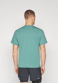 Teekinen urheilupaita lyhyillä hihoilla ja pyöreällä kaula-aukolla, jossa on hienovarainen rakenne ja logotieto takana. Kevyt kangas.