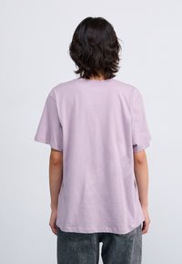 Lavender cotton t-shirt with a relaxed fit, short sleeves, and a round neckline. The fabric has a smooth texture and is displayed from the back.