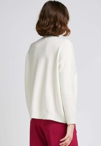 Pull blanc surdimensionné en matière douce, avec des épaulettes tombantes et des poignets côtelés, associé à un pantalon bordeaux.