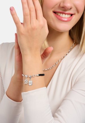 Silberarmband mit Charms, darunter "18" und ein Anhänger. Es hat schwarze Perlen, ein verlinktes Design und eine polierte Oberfläche, getragen an einem Handgelenk.