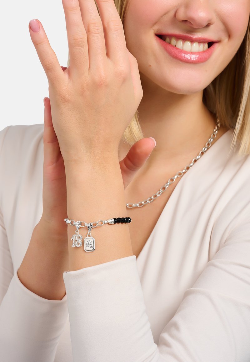 Silberarmband mit Charms, darunter "18" und ein Anhänger. Es hat schwarze Perlen, ein verlinktes Design und eine polierte Oberfläche, getragen an einem Handgelenk.