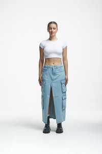 Denim krilo s križnim razporkom, ki ima velike stranske žepke, svetlo modre barve, nosi pa se z oprijetim belim crop topom in črnimi škornji.