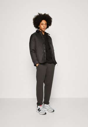 Black puffer jacket with a smooth texture, zip closure, and hood, paired with a black top and grey tapered pants. White and black sneakers.