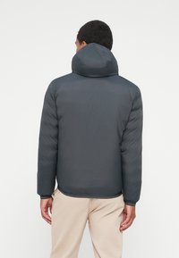 Giacca imbottita grigio scuro con cappuccio, design trapuntato, polsini elasticizzati e orlo leggermente curvo, vista da dietro.