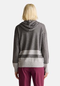 Šedá pletená mikina s kapucí a žebrovaným lemem a manžetami, s lehkými šedými pruhy uprostřed. Měkká struktura, nastavitelná kapuce, volný střih.