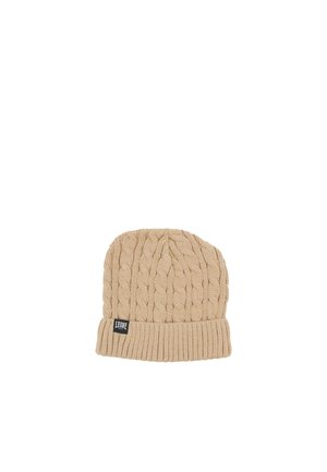 Bonnet beige en maille torsadée, avec un large revers côtelé et une petite étiquette de marque noire, sur fond blanc.