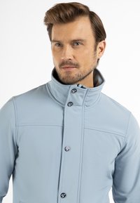 Svetlo modra softshell jakna z visokim ovratnikom, sprednjim gumbnim zapiranjem in dekorativnim šivanjem. Gladka tekstura, strukturiran dizajn in kontrastna podloga.